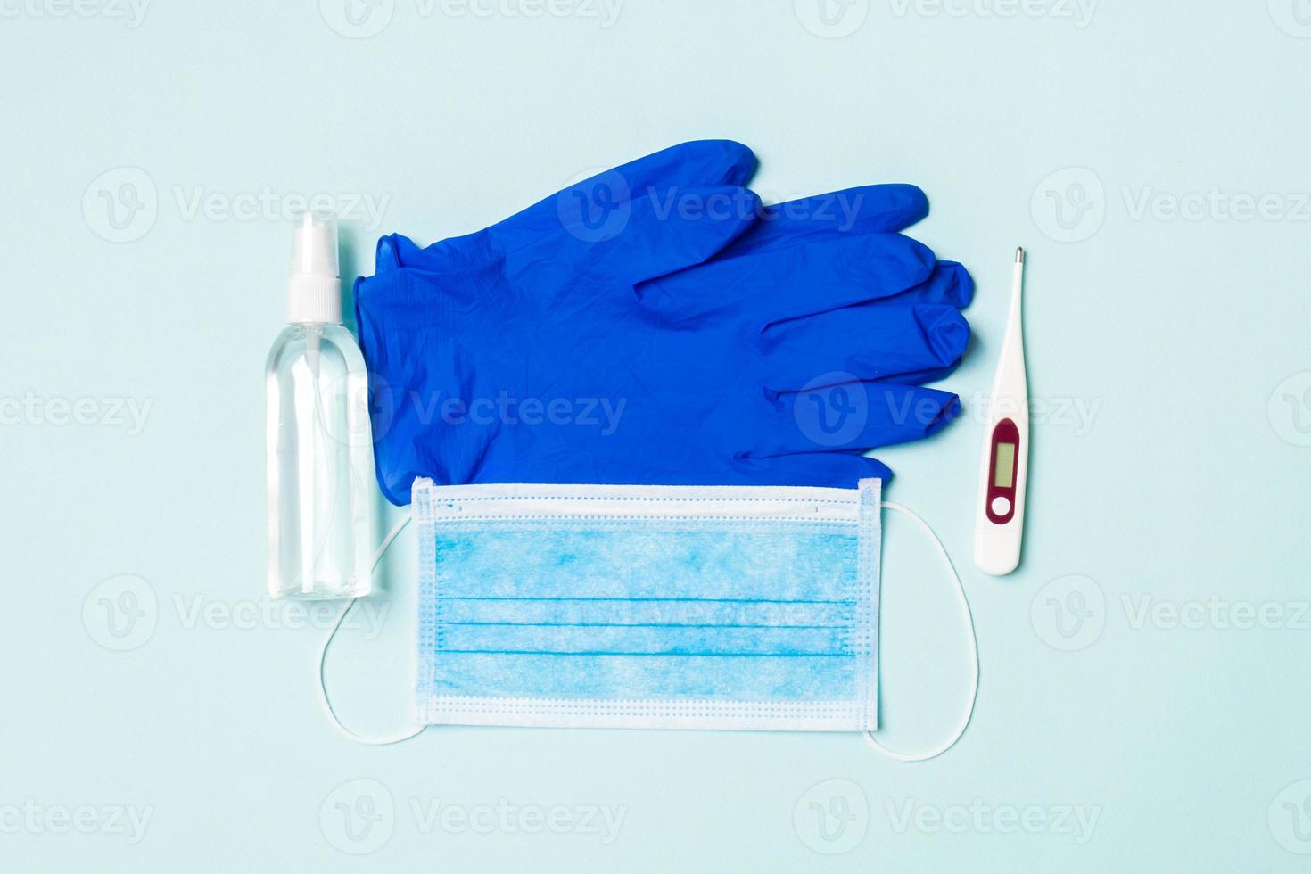 Top view of alcohol hand sanitizer, latex gloves, digital thermometer and medical mask on blue background. Virus protection equipment concept with copy space photo