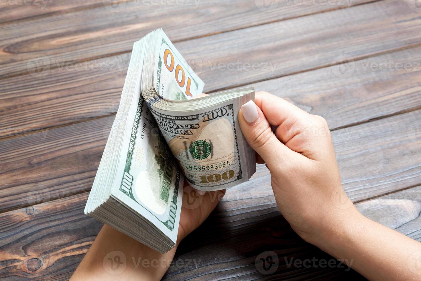 Perspective view of a businesswoman's hands counting one hundred dollar banknotes on wooden background. Success and wealth concept photo