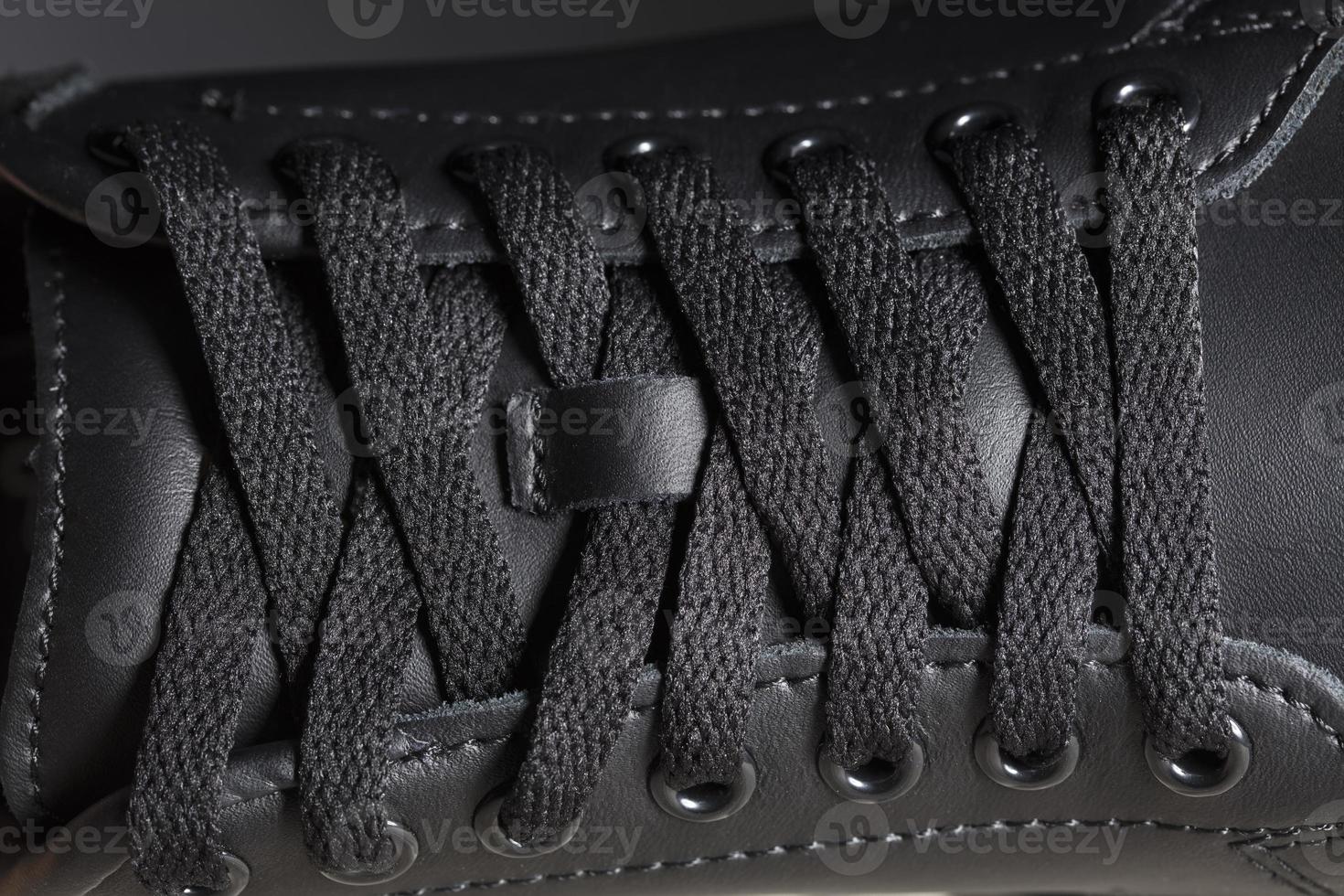 Part of a black boot with laces. A fragment of dark shoes. A piece of sneaker. photo