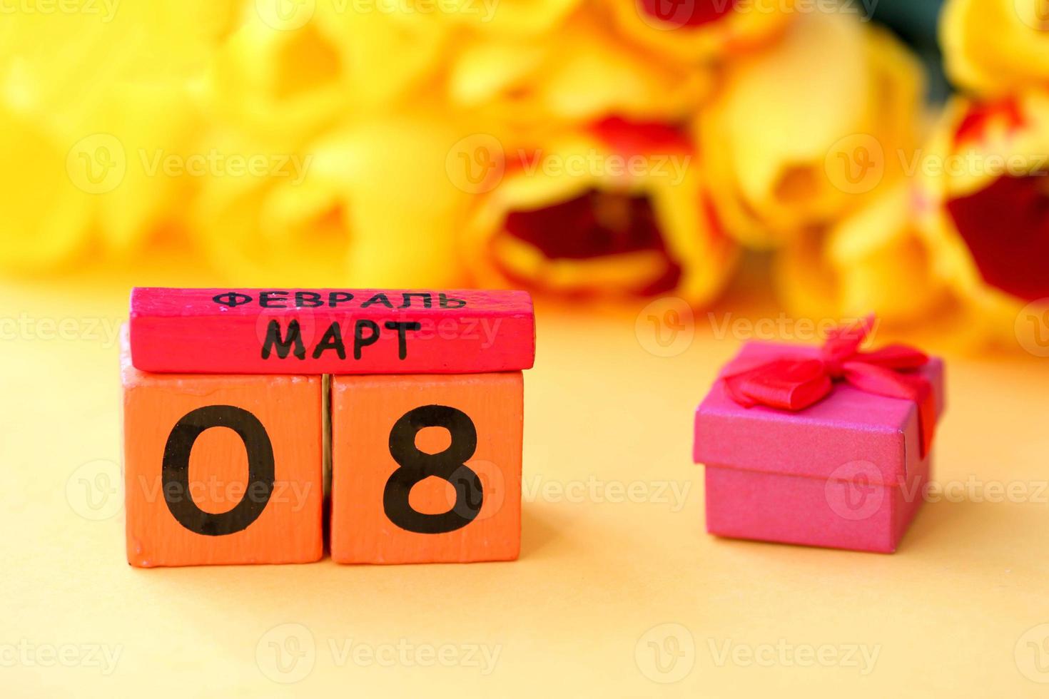 Wooden calendar with number 8 and a small red box on a background of yellow tulips. Russian text March 8. International Women is Day 8 March. photo