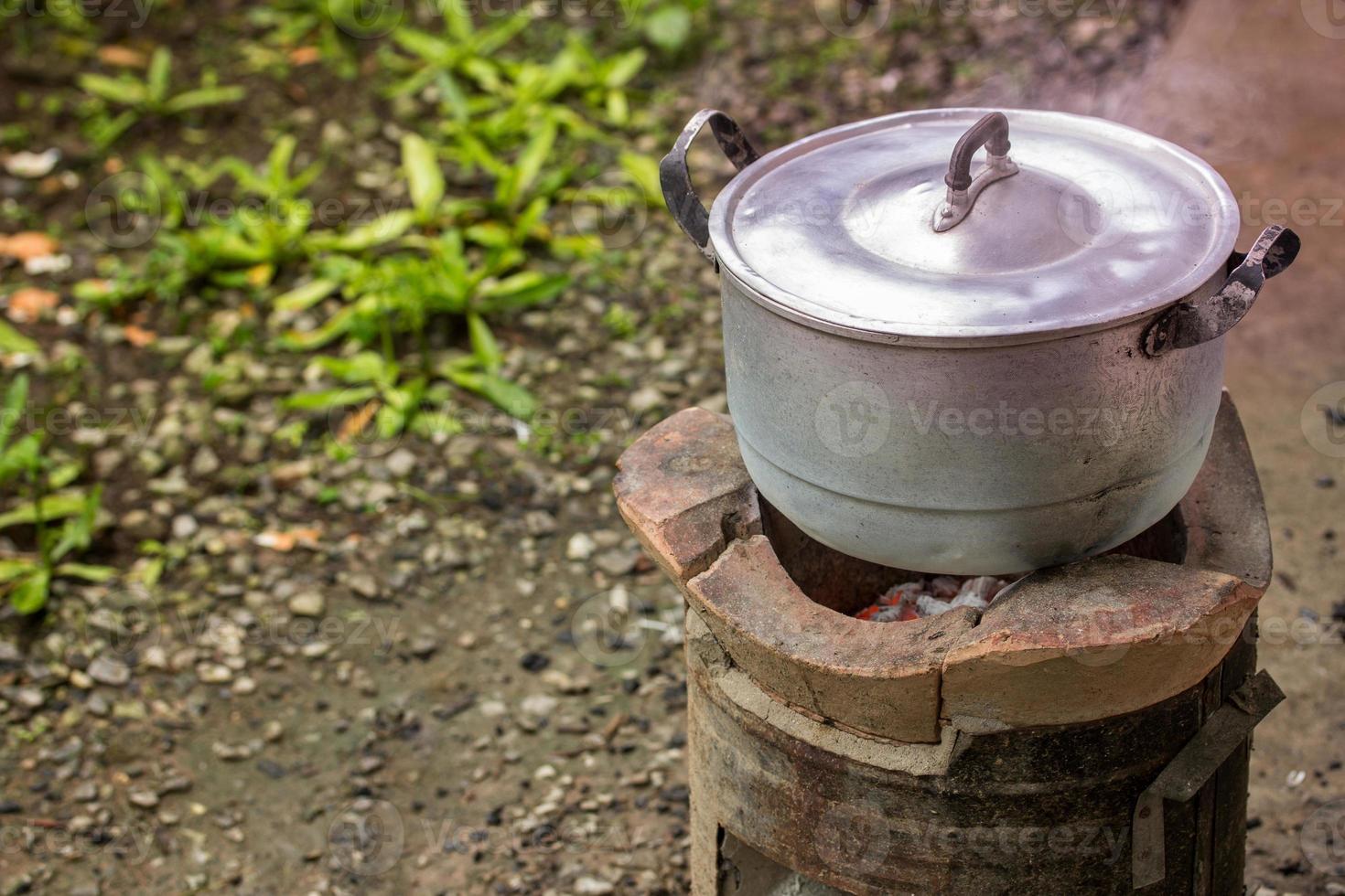 Old dirty cooking pot and bowl boiled water with steam on charcoal stove photo