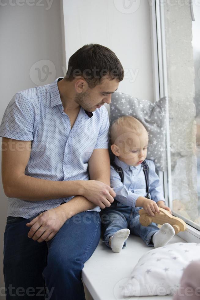 Father and little son are looking out the window. A man is playing with a child photo