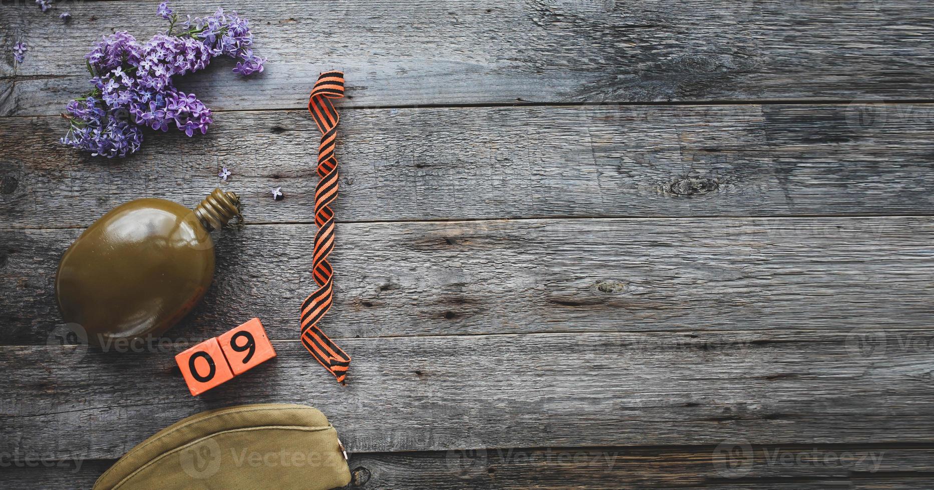 Flask, george ribbon, garrison cap and lilacs on a wooden background. Wooden calendar with date 9 May. Victory Day. Copy space. photo