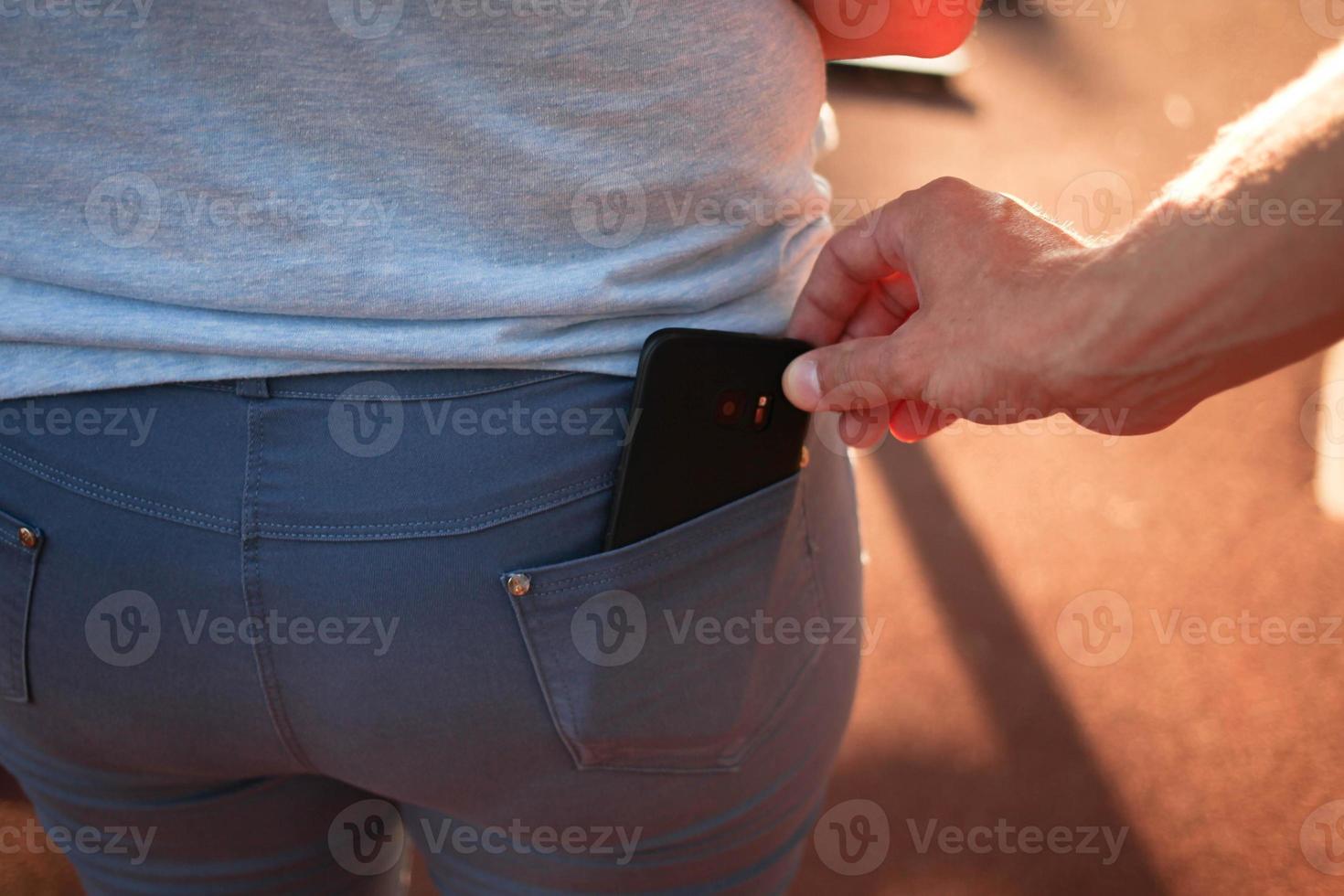 de cerca de un hombre es mano roba un móvil teléfono con un pantalones bolsillo. foto