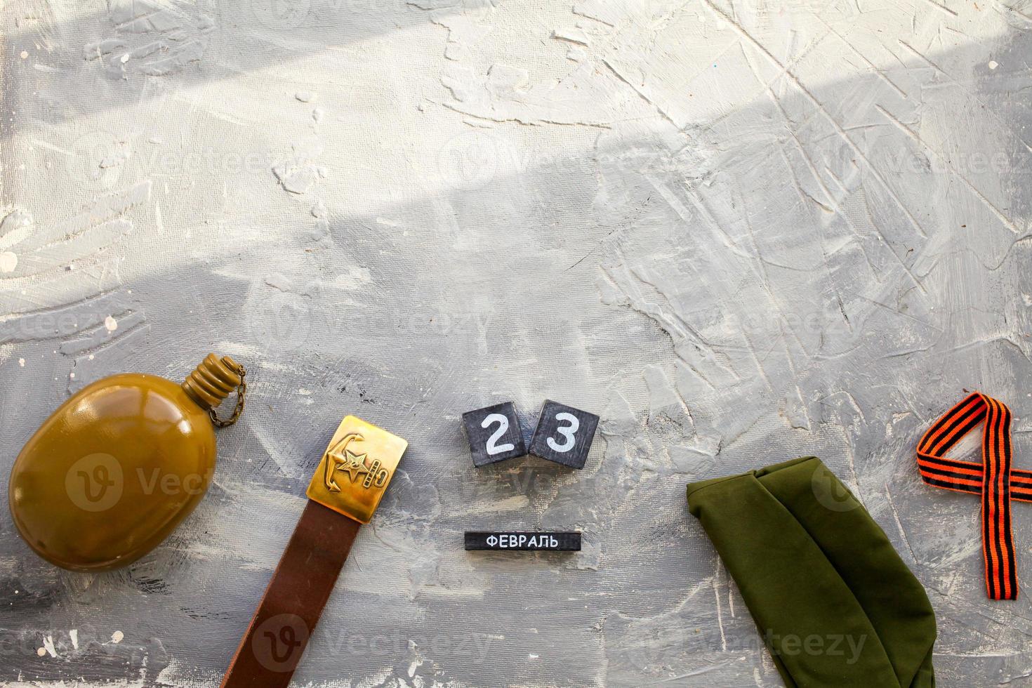 Flask, cap , george ribbon, soldier belt with a five-pointed star with a hammer and sickle and a wooden calendar with the date February 23. Fatherland defender day. Text in Russian photo