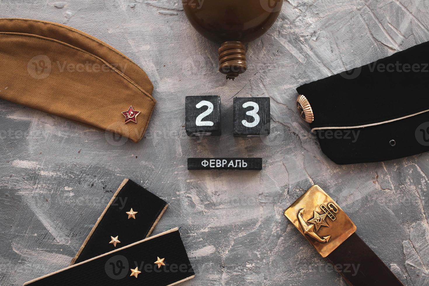 Flask, cap, army belt depicting a hammer and shoulder straps  of the war years and a wooden calendar with the date . Fatherland defender day.  Text in Russian February 23. photo