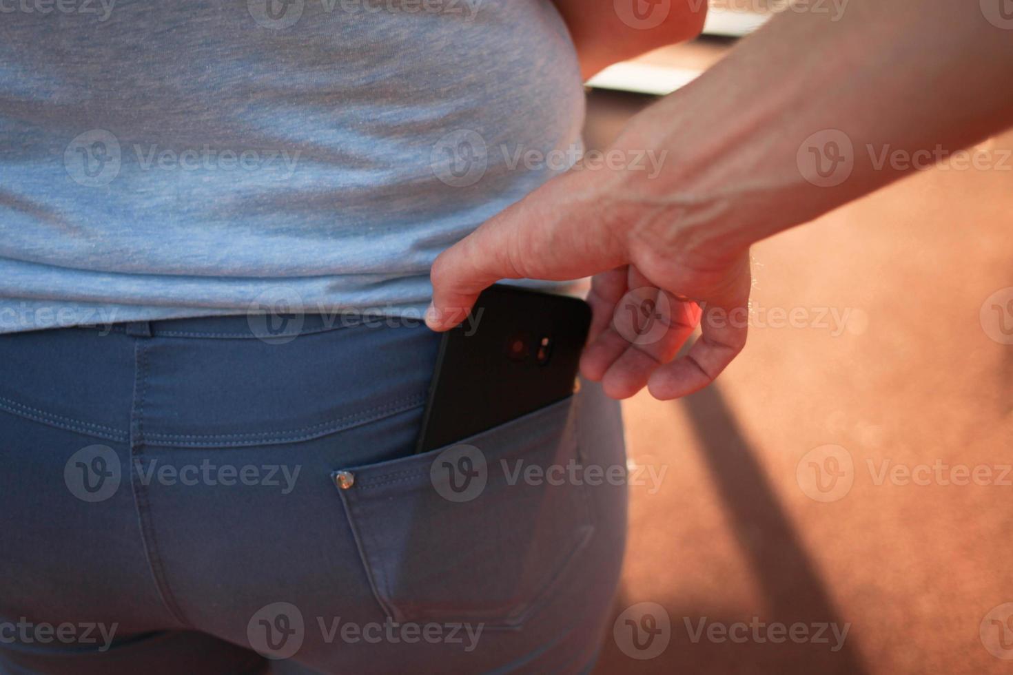 de cerca de un hombre es mano roba un móvil teléfono con un pantalones bolsillo. foto