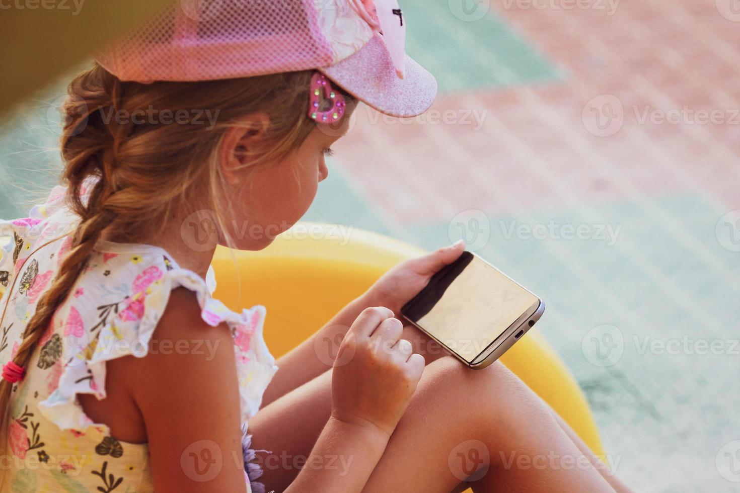 The girl sits on the playground and plays games on the phone. Internet addiction, loneliness. photo