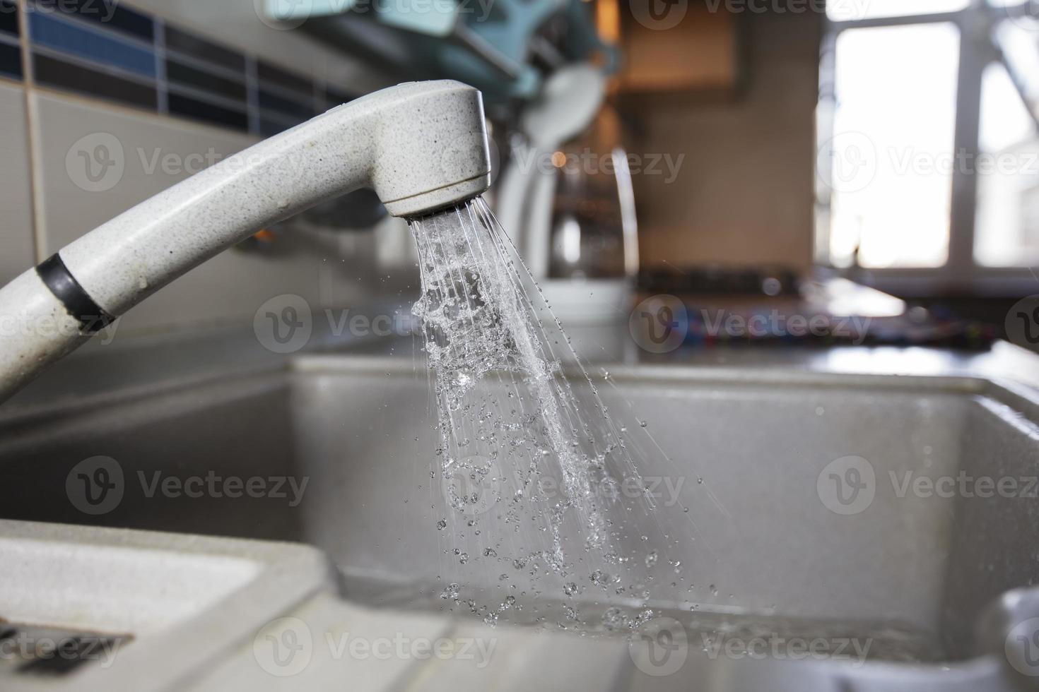 Water is pouring from a faucet. Water tap on the background of the kitchen. House water consumption. photo