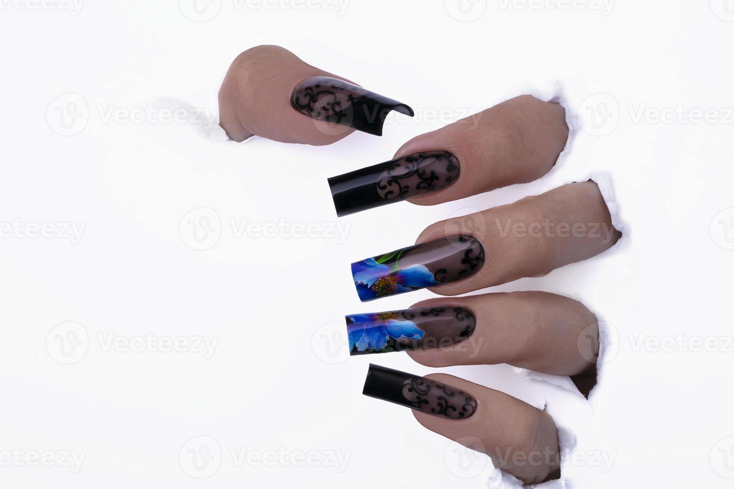 Fingers with a beautiful manicure in a hole in the paper. photo