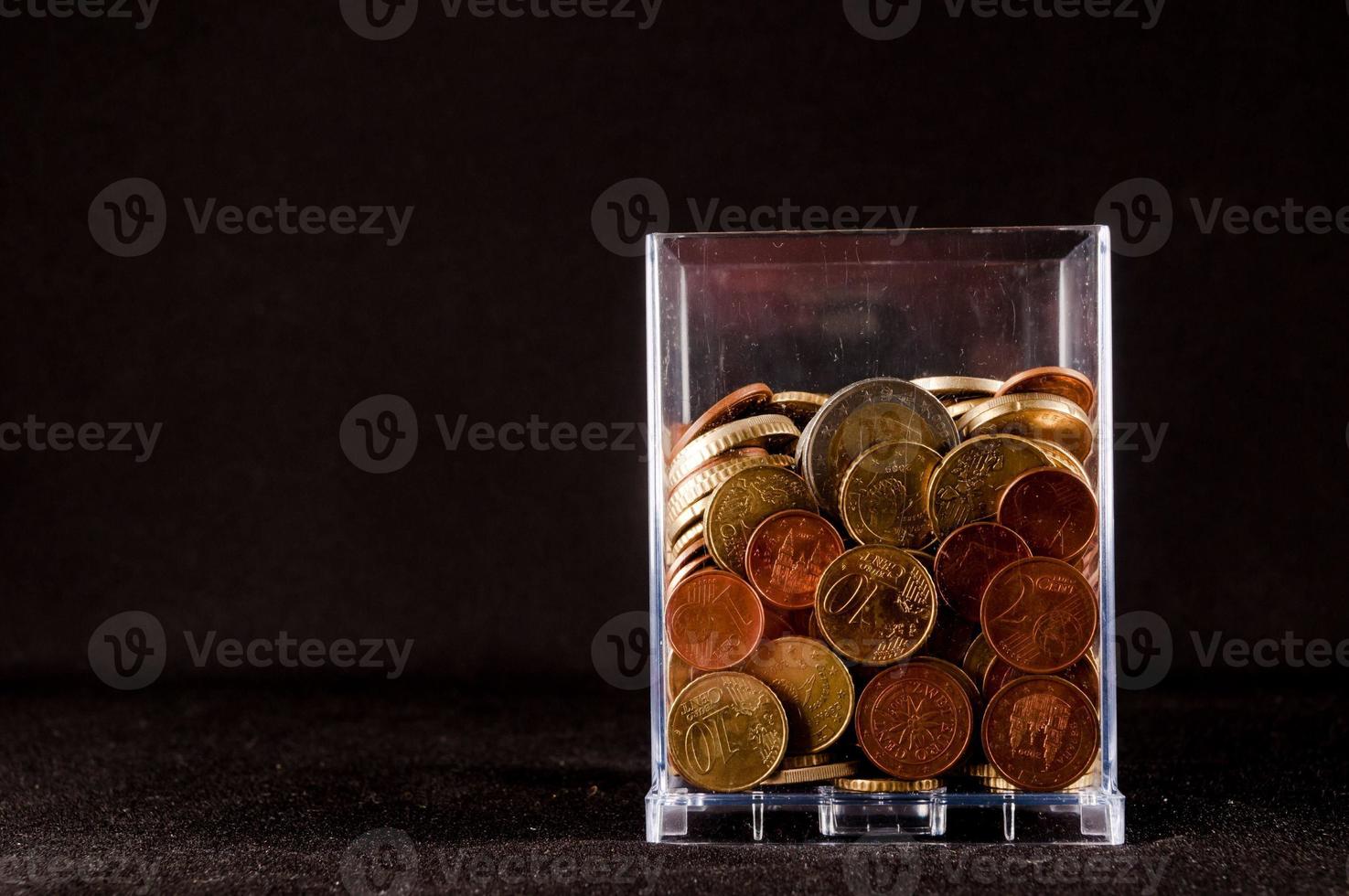 Glass with coins isolated on black background photo