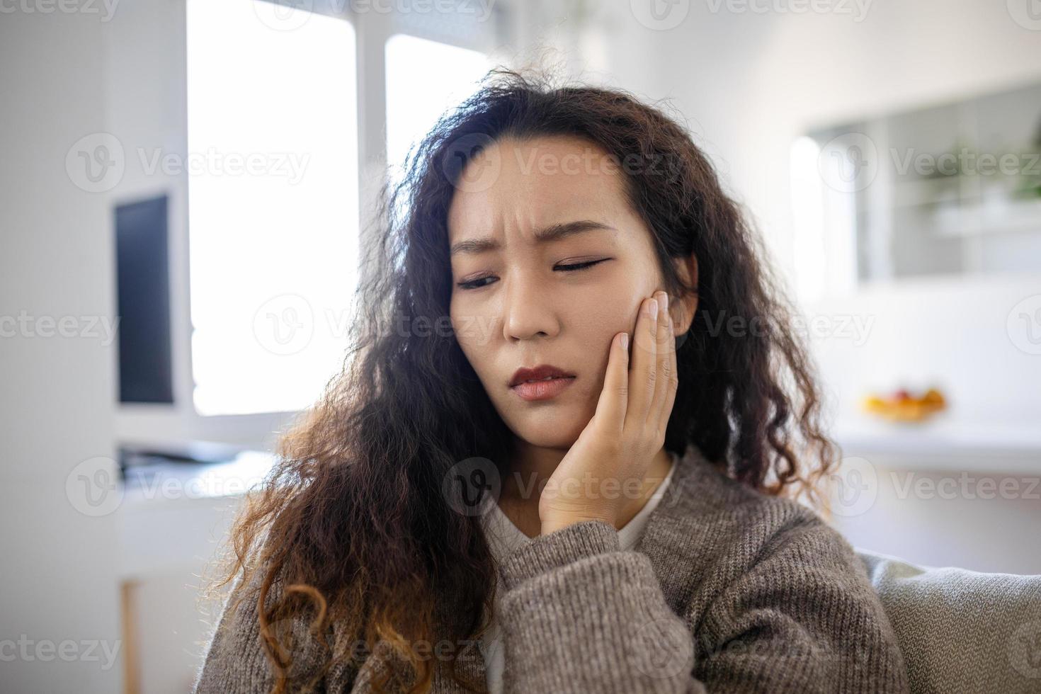 Portrait of unhappy young Asian woman suffering from toothache at home. Healthcare, dental health and problem concept. photo