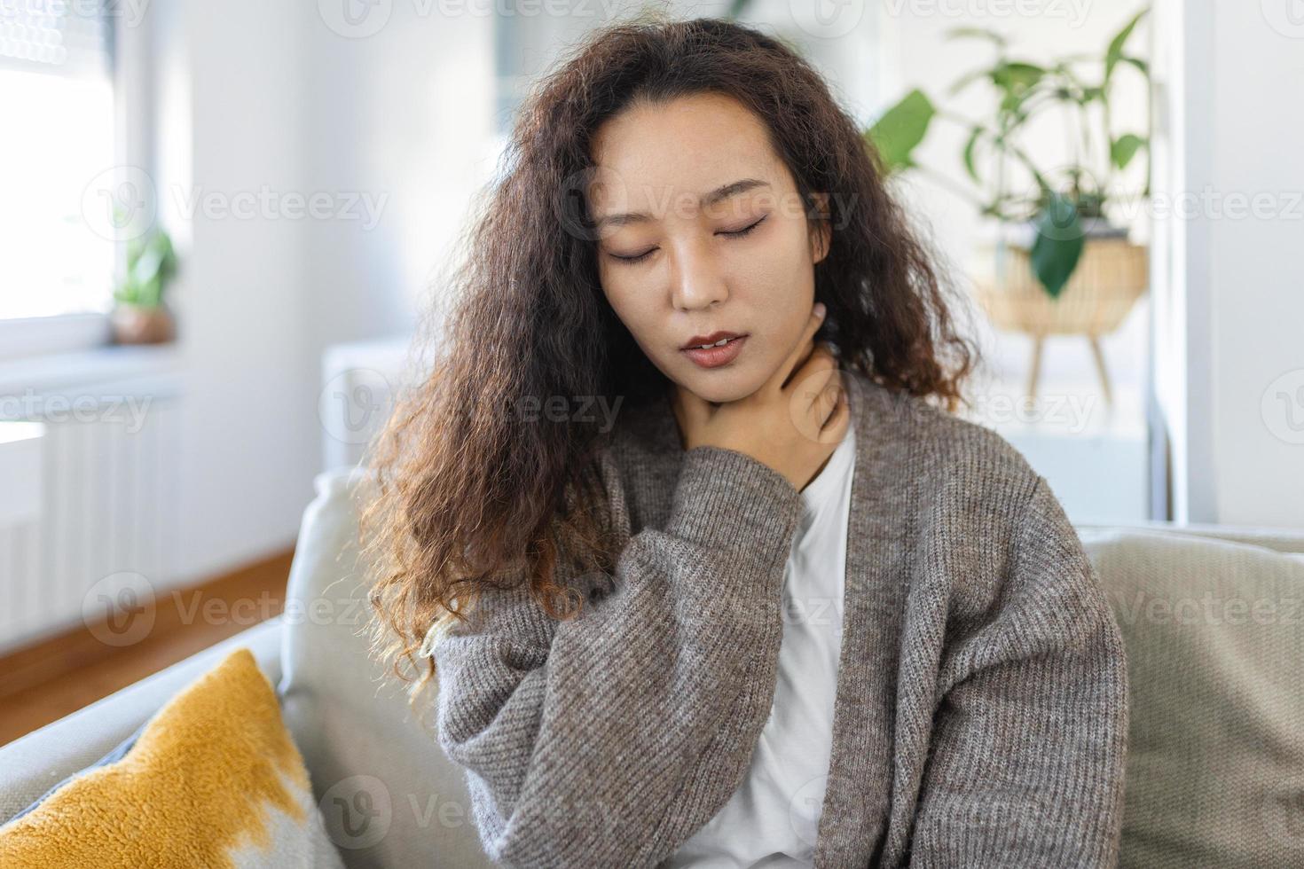 Close up of young Asian woman rubbing her inflamed tonsils, tonsilitis problem, cropped. Woman with thyroid gland problem, touching her neck, girl has a sore throat photo