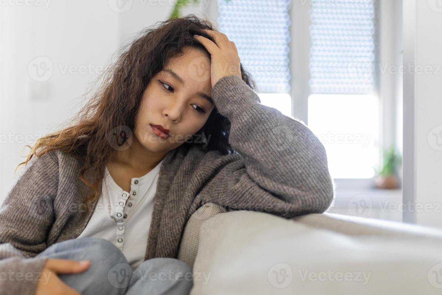 infeliz asiático mujer en sofá llanto. solitario triste mujer profundo en pensamientos sentado soñador o esperando para alguien en el vivo habitación con un grave expresión, sentado en sofá foto