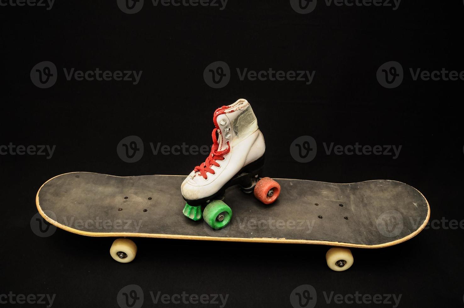 Skateboard and roller skate on black background photo