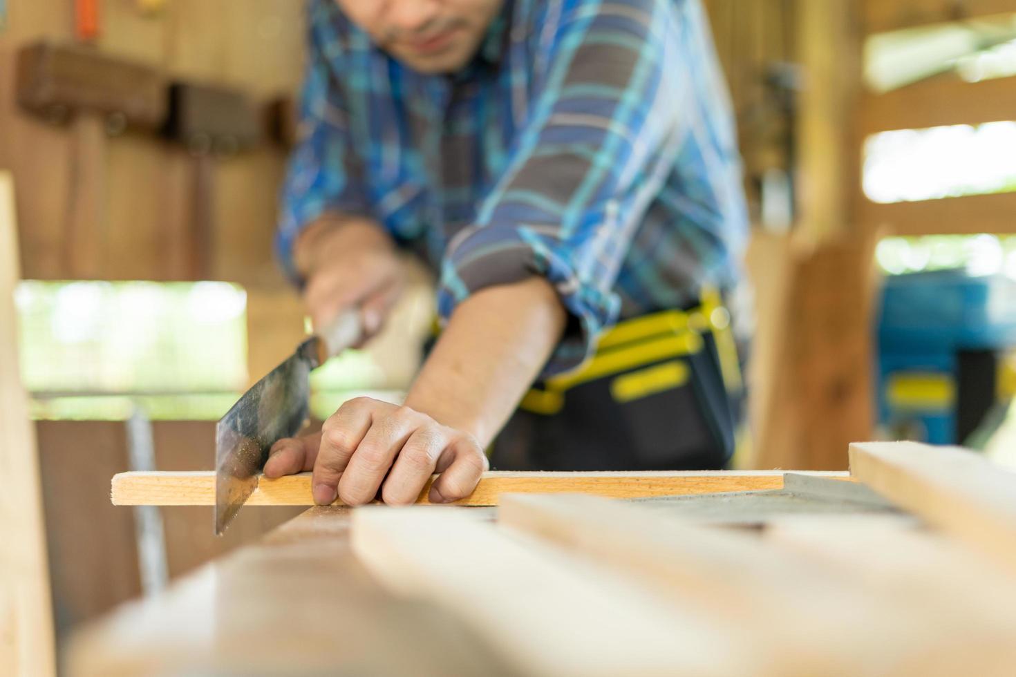 asiático hombre propietario un pequeño mueble negocio es preparando madera para producción. carpintero masculino es ajustar madera a el deseado tamaño. arquitecto, diseñador, incorporado, profesional madera, artesano, taller. foto