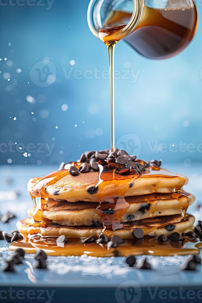 Syrup is poured down and chocolate chips are on top tall stack of golden pancakes layered on a plate with melted butter and syrup dripping down the sides of the stack. . photo