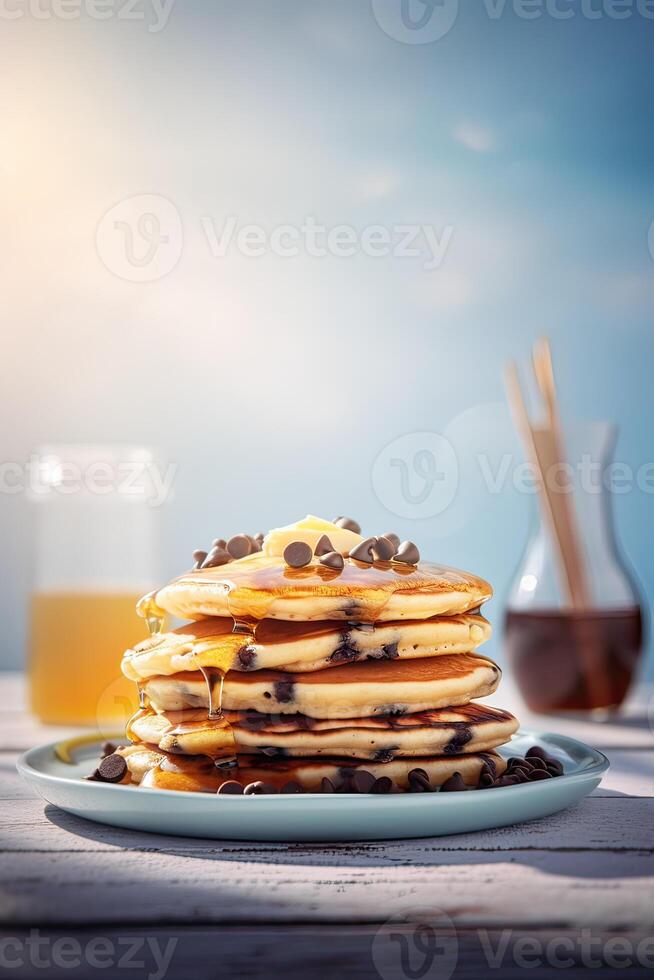 Syrup is poured down and chocolate chips are on top tall stack of golden pancakes layered on a plate with melted butter and syrup dripping down the sides of the stack. . photo