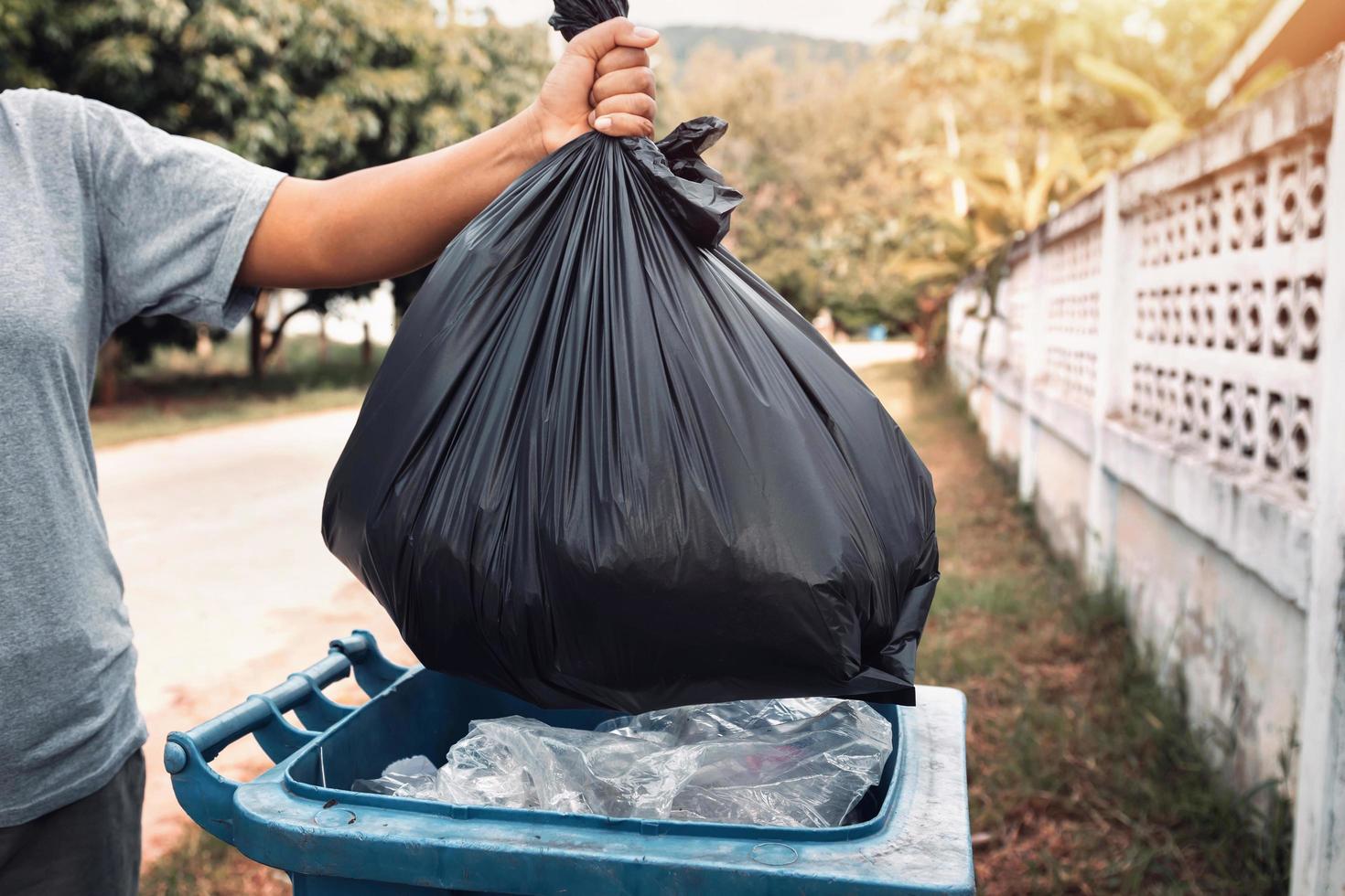 mujer mano participación basura en negro bolso para limpieza en a basura foto