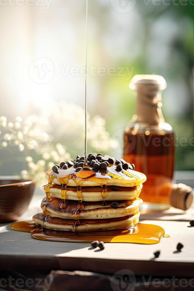 Syrup is poured down and chocolate chips are on top tall stack of golden pancakes layered on a plate with melted butter and syrup dripping down the sides of the stack. . photo