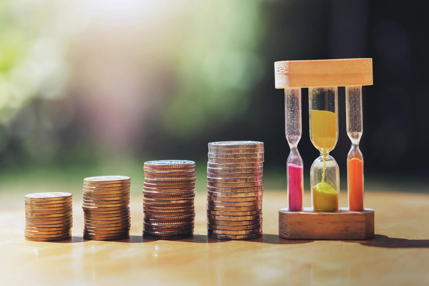 dinero apilar con reloj de arena en mesa y puesta de sol foto