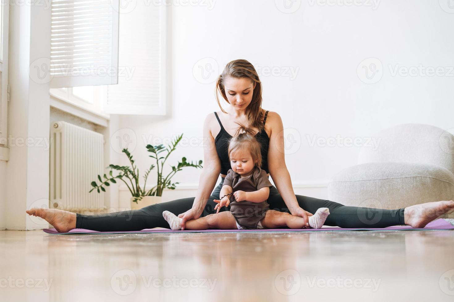 mujer joven en forma mamá con niña haciendo fitness en la alfombra en casa foto