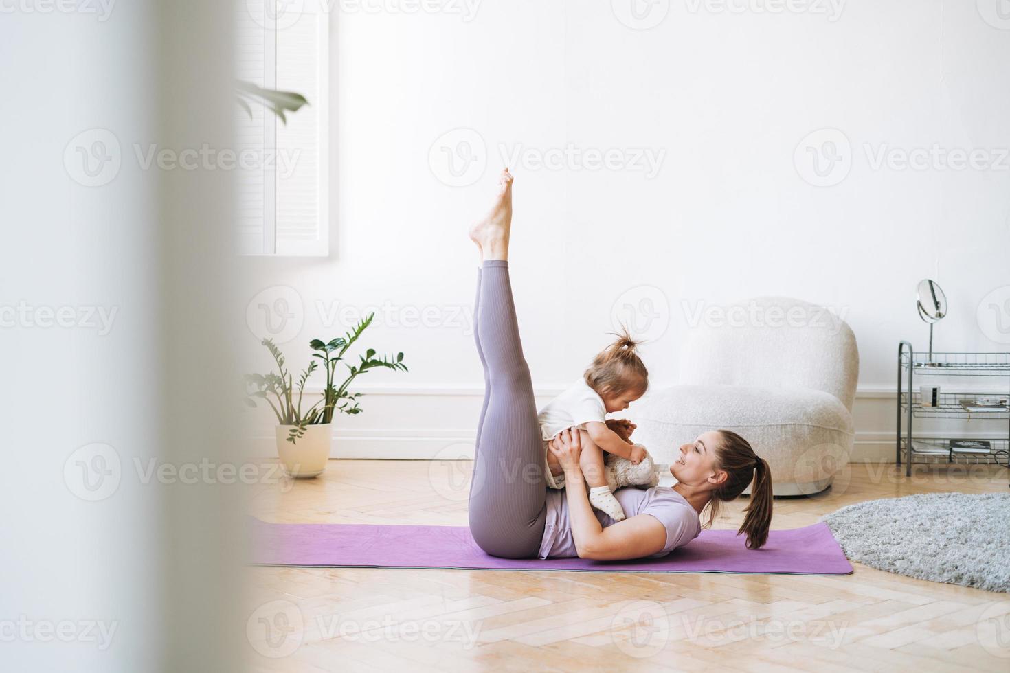 mujer joven en forma mamá con niña haciendo fitness en la alfombra en casa foto