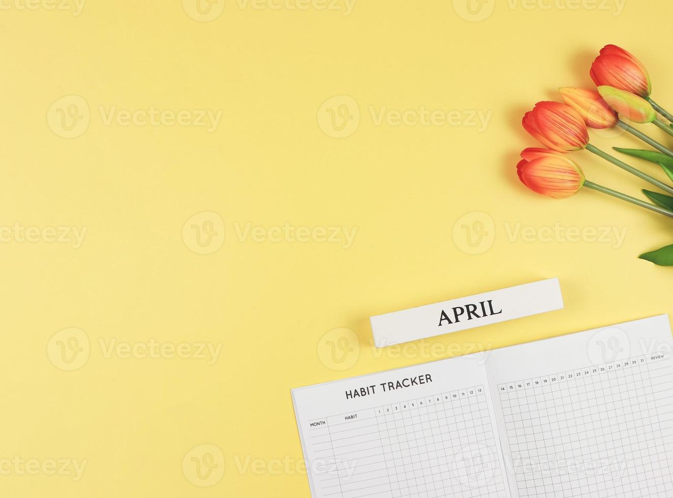 flat layout of Habit tracker book, wooden calendar April,  and tulips on yellow background with copy space. photo