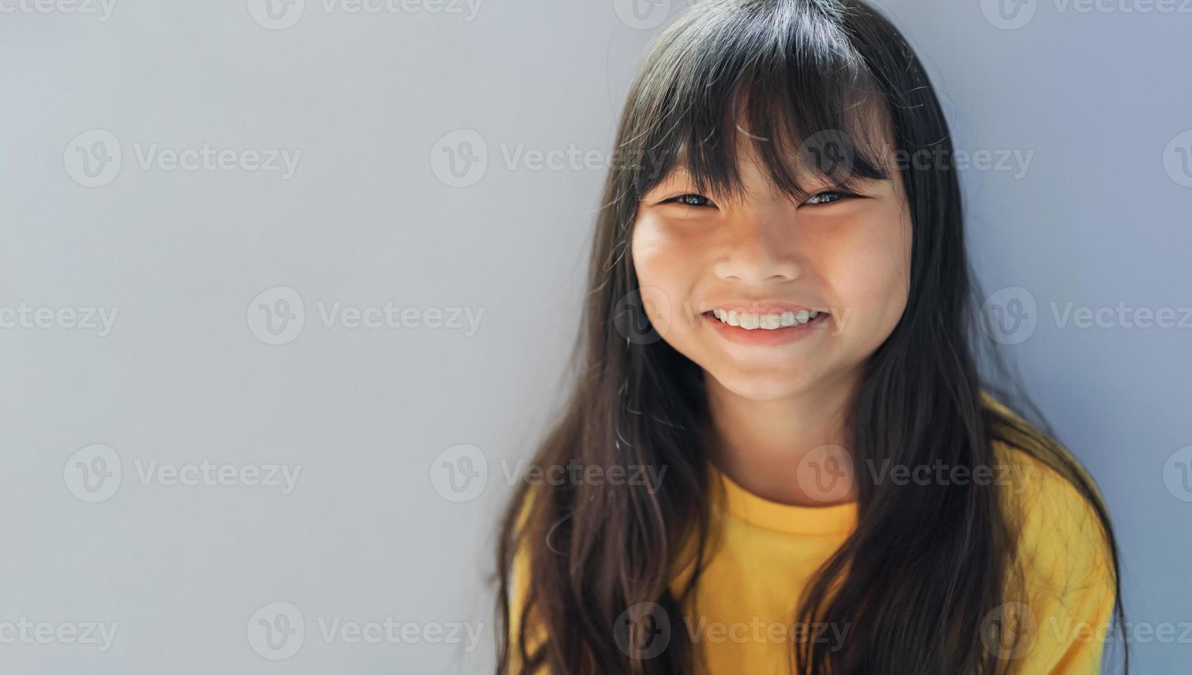 linda pequeño niña sonriente en gris antecedentes foto