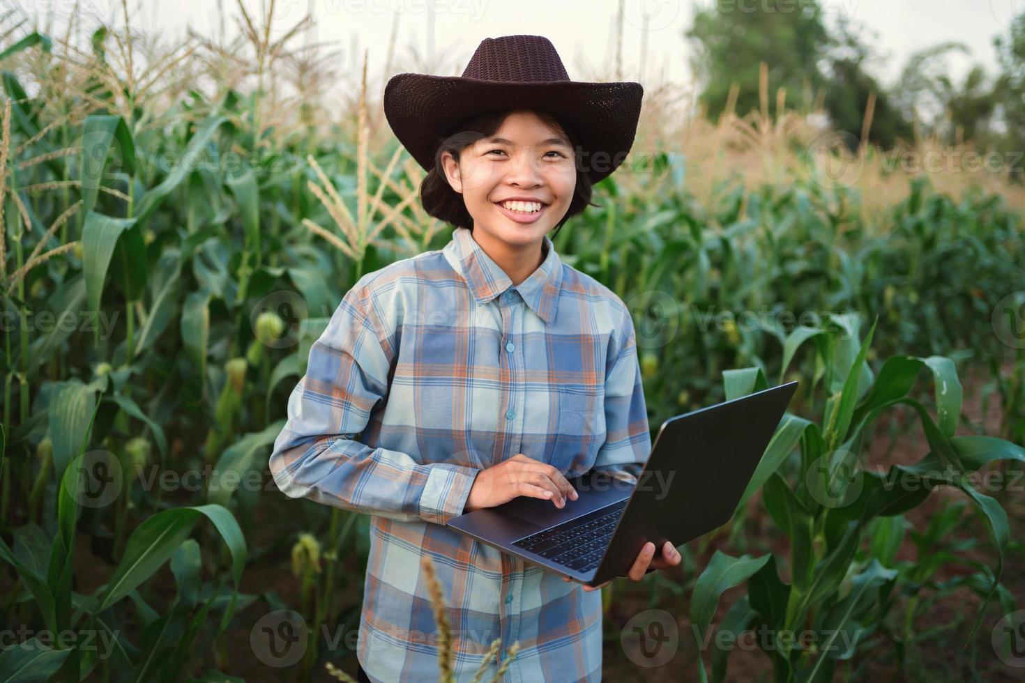 young woman standing use laptop checking corn in farm. technology agriculture conept photo