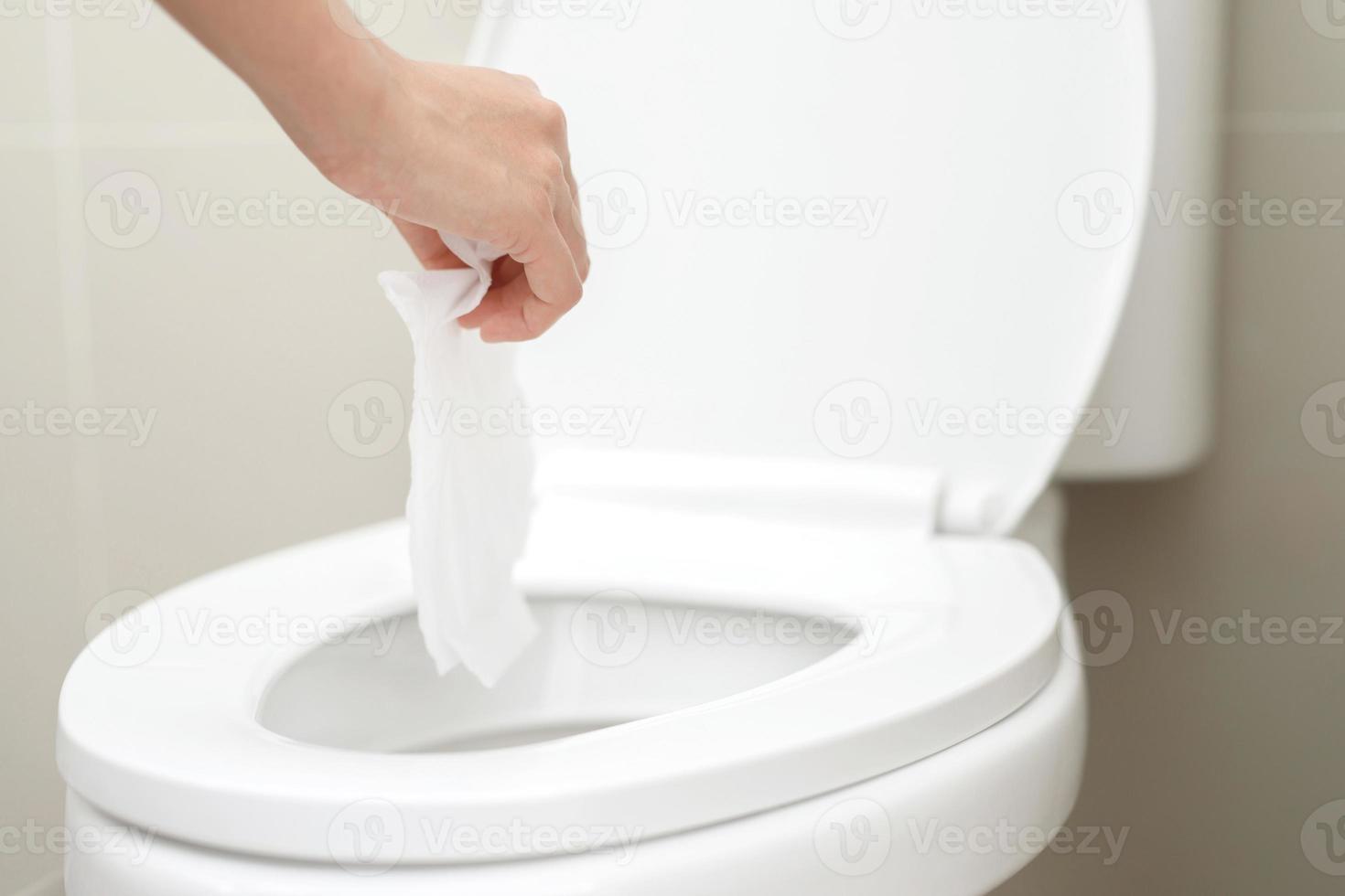 close up hand holding a tissue to be thrown into the toilet bowl. Can not drain water of toilet paper in the toilet bowl cause the stool to clog up. photo