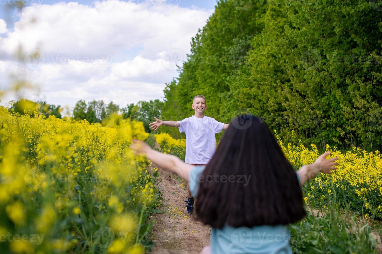 un linda chico en un blanco camiseta carreras a su madre en un colza campo foto