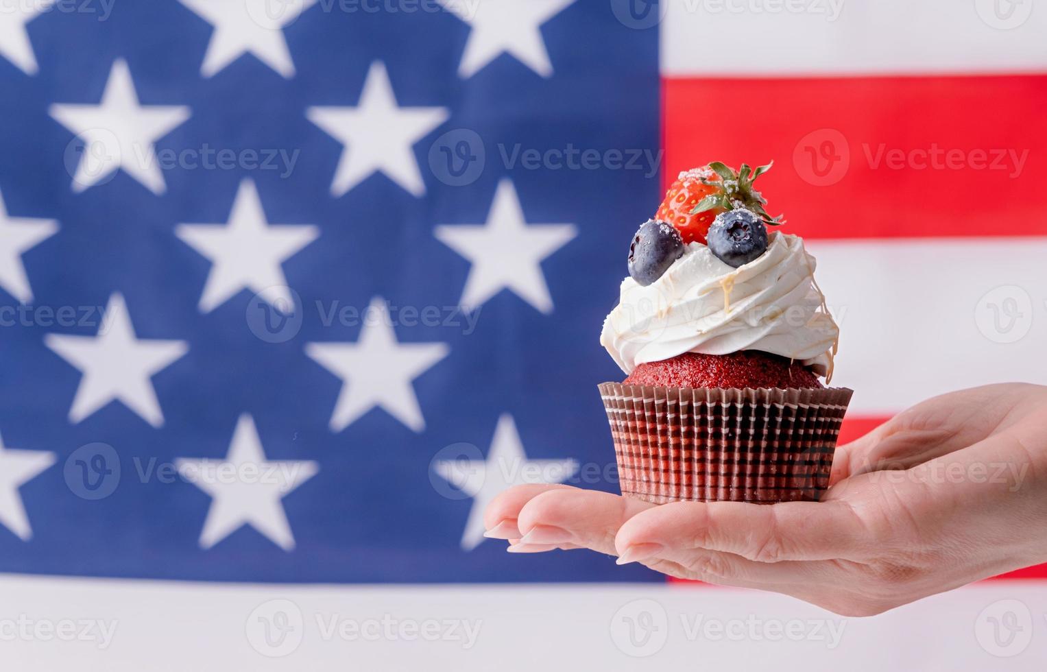 hand holding sweet cupcake with blueberries and strawberry , flag background photo