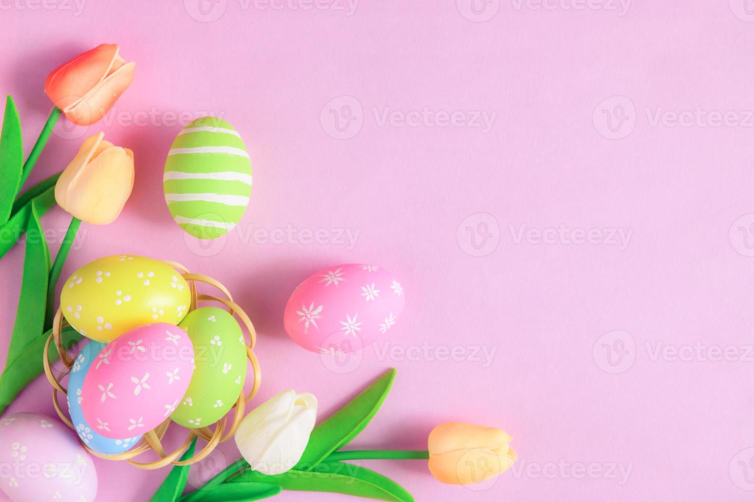 Happy Easter holiday greeting card concept. Colorful Easter Eggs and spring flowers on pastel pink background. Flat lay, top view, copy space. photo