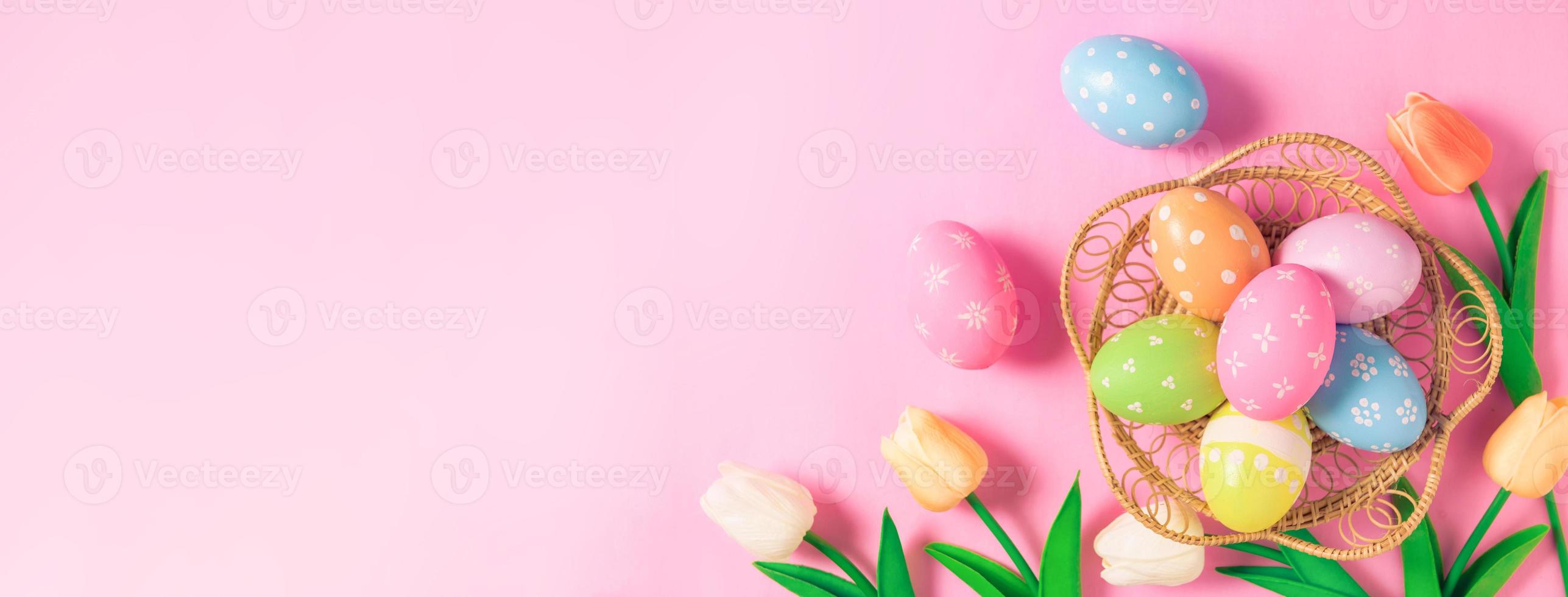 Happy Easter holiday greeting card concept. Colorful Easter Eggs and spring flowers on pastel pink background. Flat lay, top view, copy space. photo