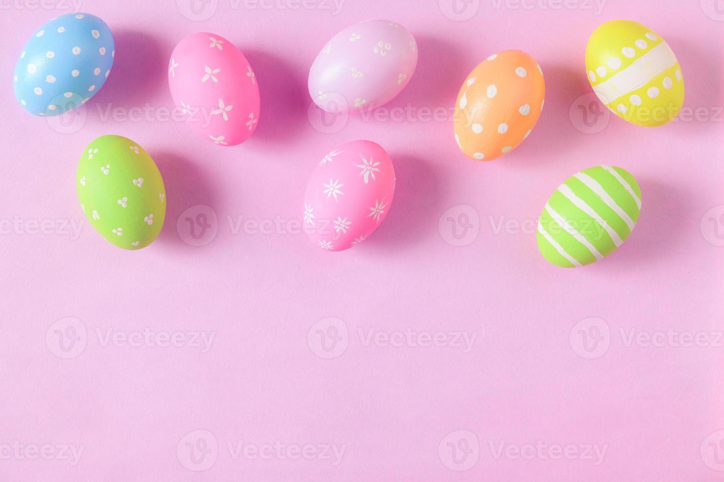 Happy Easter holiday greeting card concept. Colorful Easter Eggs and spring flowers on pastel pink background. Flat lay, top view, copy space. photo