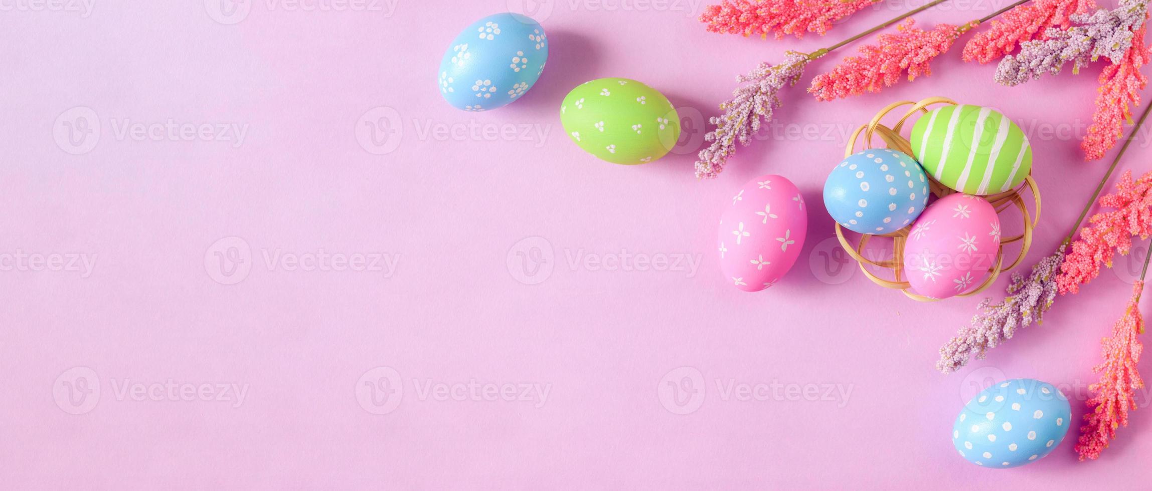Happy Easter holiday greeting card concept. Colorful Easter Eggs and spring flowers on pastel pink background. Flat lay, top view, copy space. photo