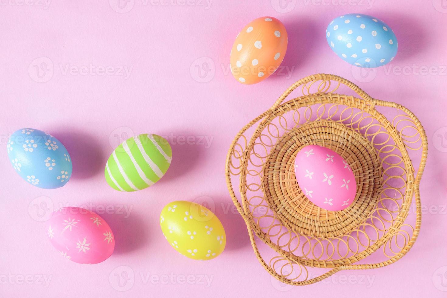Happy Easter holiday greeting card concept. Colorful Easter Eggs and spring flowers on pastel pink background. Flat lay, top view, copy space. photo