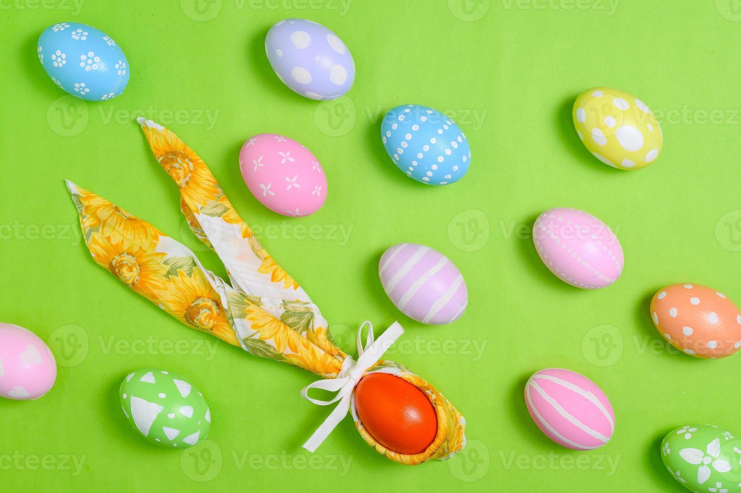 Happy Easter holiday greeting card design concept. Colorful Easter Eggs and spring flowers on pastel green background. Flat lay, top view, copy space. photo
