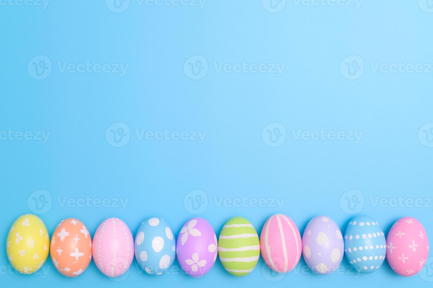 Happy Easter holiday greeting card design concept. Colorful Easter Eggs and spring flowers on blue background. Flat lay, top view, copy space. photo