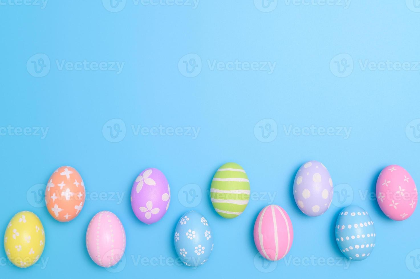 Happy Easter holiday greeting card design concept. Colorful Easter Eggs and spring flowers on blue background. Flat lay, top view, copy space. photo