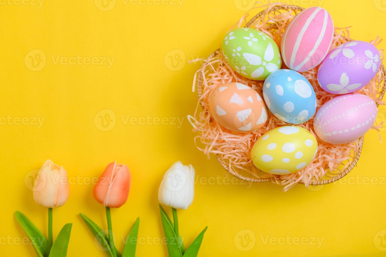 Happy Easter holiday greeting card design concept. Colorful Easter Eggs and spring flowers on yellow background. Flat lay, top view, copy space. photo