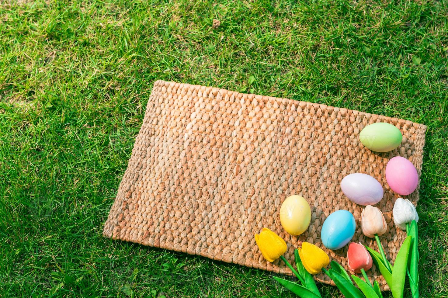 Happy Easter holiday greeting card concept. Colorful Easter Eggs and spring flowers on Papyrus rattan weave texture background. Flat lay, top view, copy space. photo