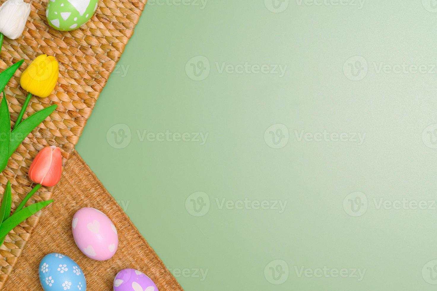 Happy Easter holiday greeting card design concept. Colorful Easter Eggs and spring flowers on pastel green background. Flat lay, top view, copy space. photo