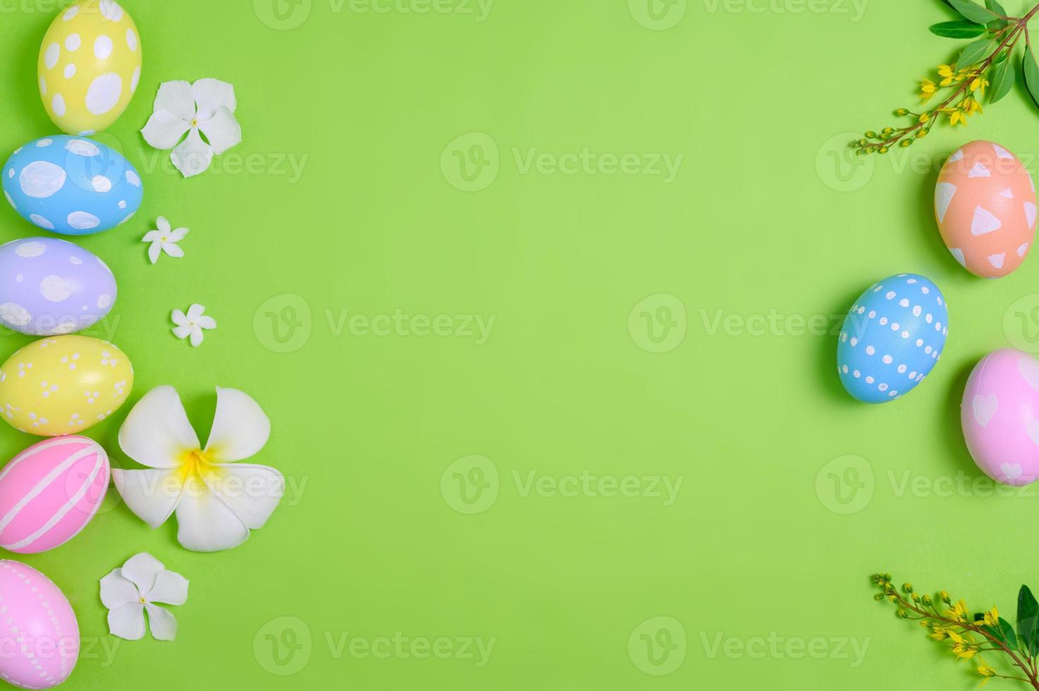 Happy Easter holiday greeting card design concept. Colorful Easter Eggs and spring flowers on pastel green background. Flat lay, top view, copy space. photo