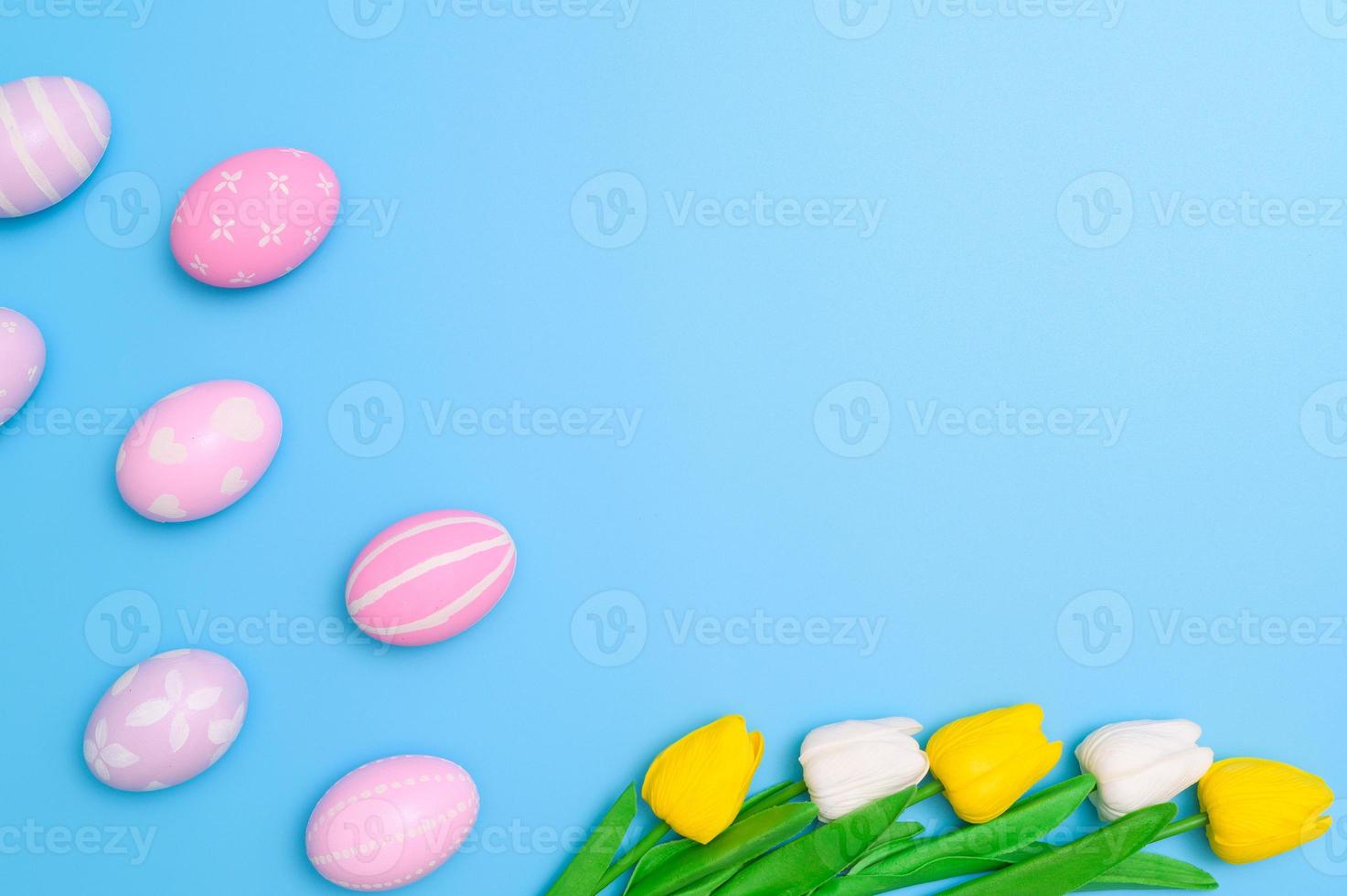 Happy Easter holiday greeting card design concept. Colorful Easter Eggs and spring flowers on blue background. Flat lay, top view, copy space. photo