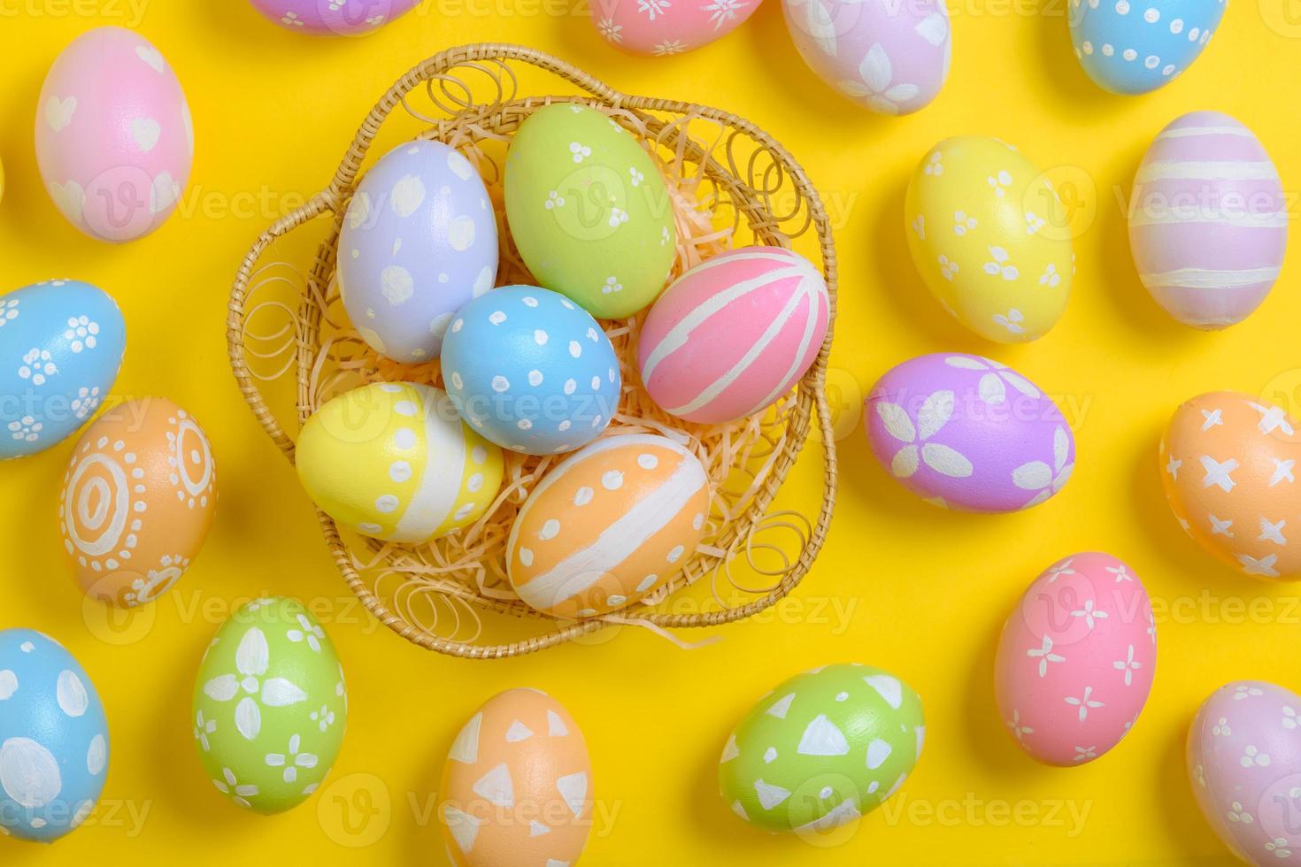 Happy easter celebration holiday. colourful pastel painted eggs in wicker basket nest decoration on a yellow background. Seasonal greeting gift card concept. Top view, flat lay, copy space. photo