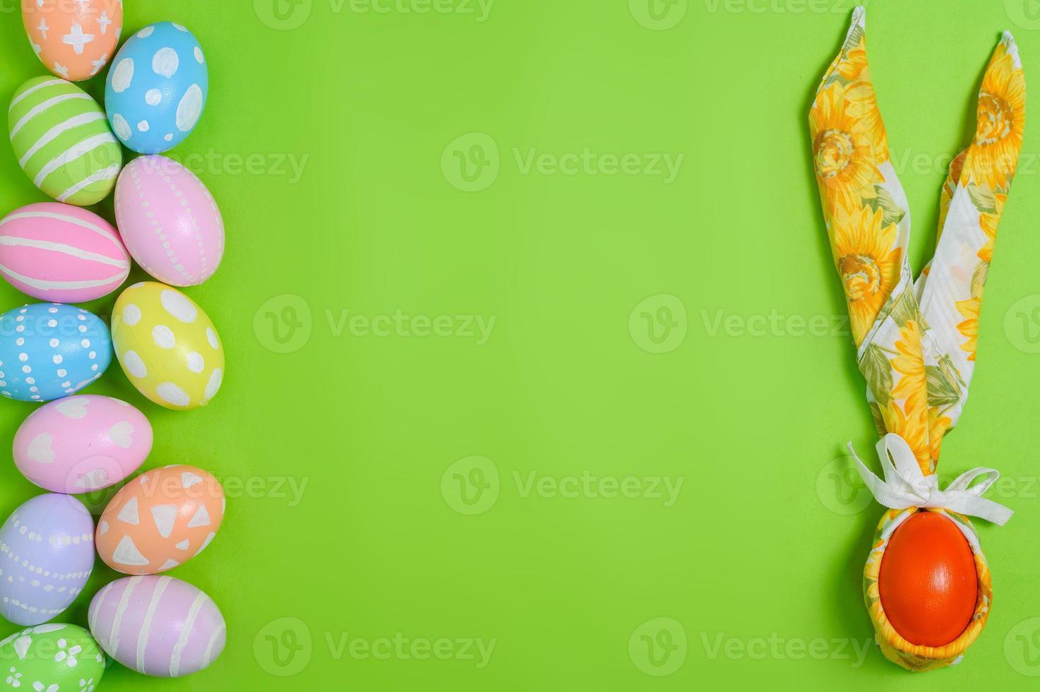 Happy Easter holiday greeting card design concept. Colorful Easter Eggs and spring flowers on pastel green background. Flat lay, top view, copy space. photo