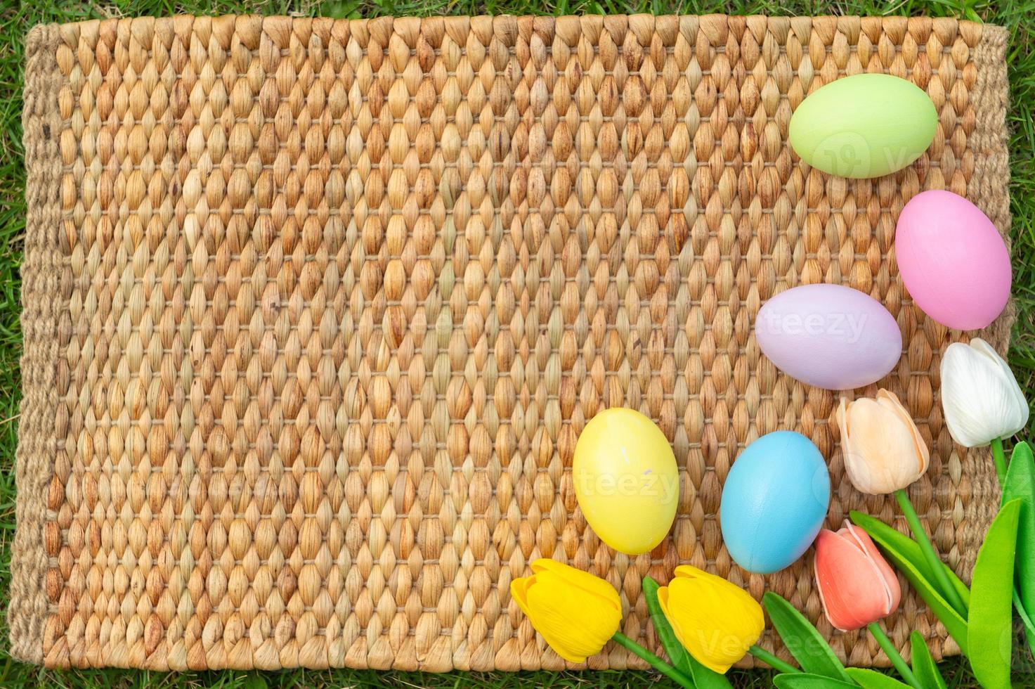 Happy Easter holiday greeting card concept. Colorful Easter Eggs and spring flowers on Papyrus rattan weave texture background. Flat lay, top view, copy space. photo