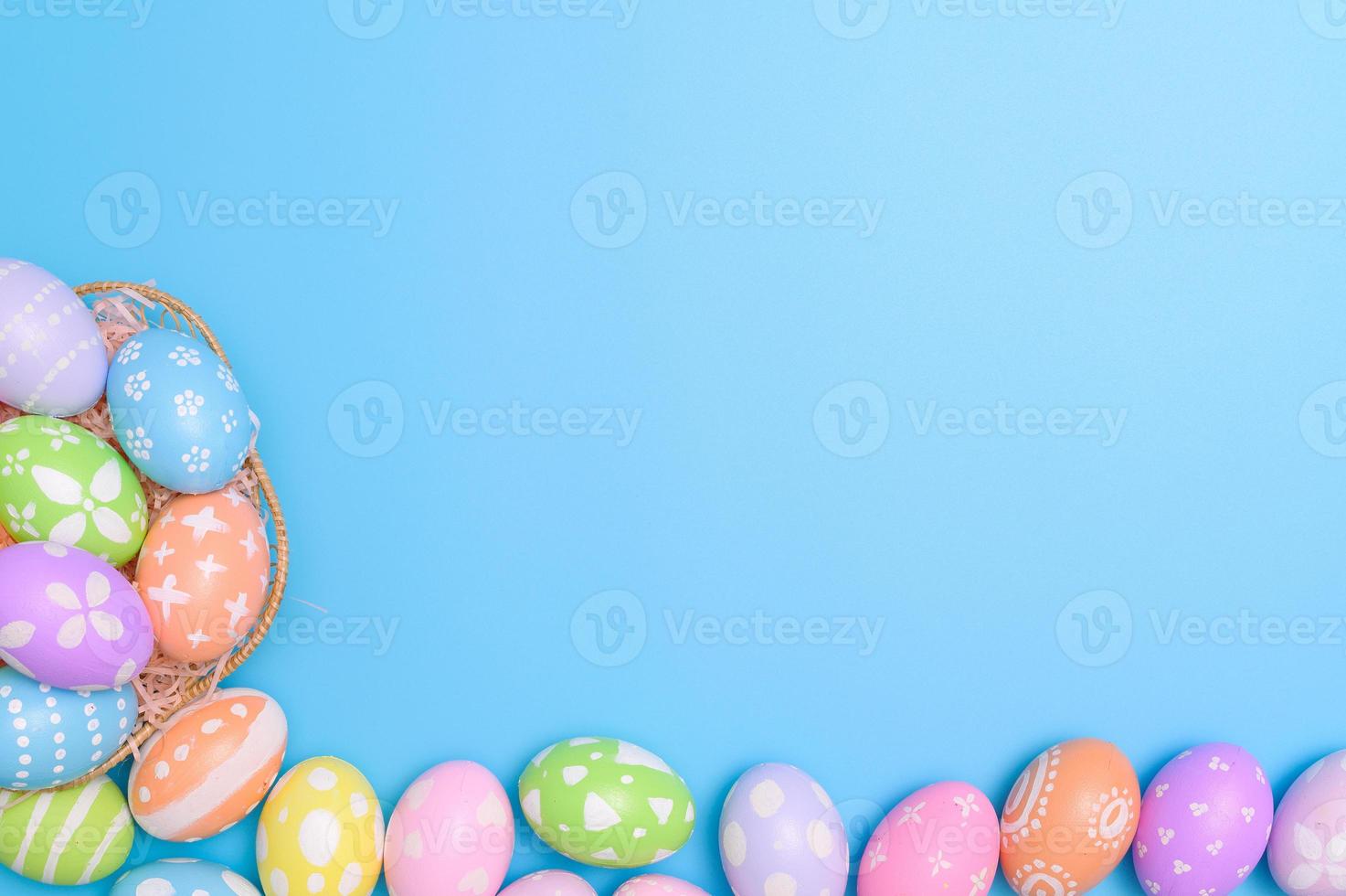 Happy Easter holiday greeting card design concept. Colorful Easter Eggs and spring flowers on blue background. Flat lay, top view, copy space. photo